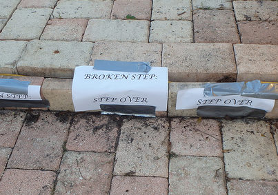 Brick steps that are broken with a sign on them that reads, "Broken step: step over."