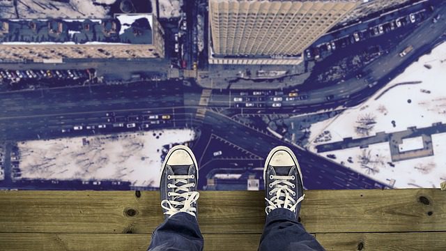 someone in a pair of lace-up tennis shoes and jeans standing on a board looking down past their feet at a city intersection