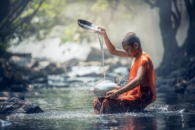 young monk sitting in river pouring water