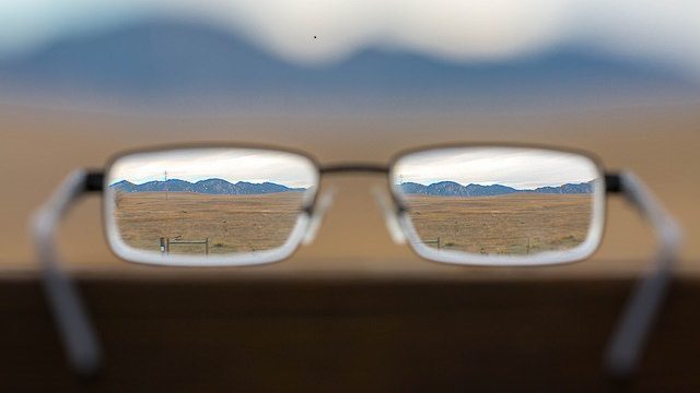 Background of blurry mountains and fields with a pair of glasses through which you see the mountains and fields clearly.